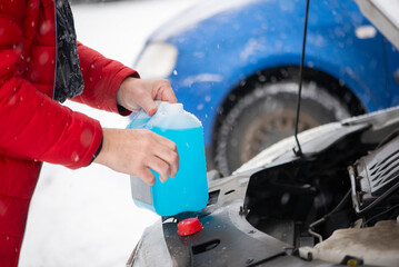 Person pouring antifreeze to the car in wintertime. Technician with open hood adding cooland to the...