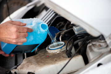 Person pouring antifreeze to the car in wintertime. Technician with open hood adding cooland to the...