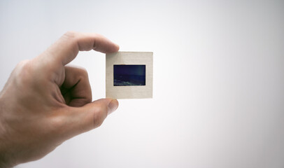 The hand holds a cardboard slide with a photo on a white isolate. The old way of storing film...
