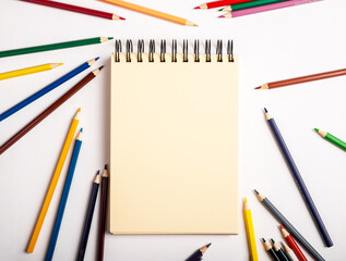 Blank paper, empty page of notebook on spirals with colored pencils around. Notepad mockup for text and drawing