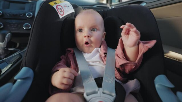 Wonder charming little girl sitting in a baby car seat feels looking around. The child is inside the car. Vehicle and transportation concept. Travel. Slow motion