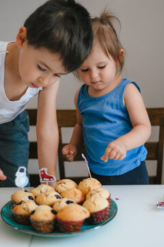 Two impatient children sitting at the kitchen table and looking at the plate full of freshly baked muffins. Closeup portrait. Baking cooking preparing surprise