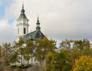 Najstarszy kościół ( rzymskokatolicki) w Ostrowcu Świętokrzyskim . Stojący na wzgórzu ponad miastem w otoczeniu jesiennych modrzewi i innych drzew . - obrazy, fototapety, plakaty