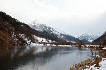 winter mountain lake in snow, in background of mountain, landscape pond with ice on water