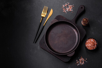 Brown iron empty pan with kitchen utensils on a dark concrete background