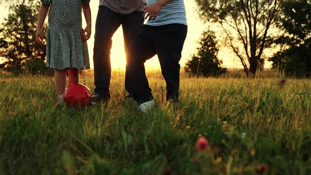 Children son daughter play football with father on lawn. Boy girl parent run after red ball in park. Family team, sports games. Active happy family, kids dad having fun playing ball on green grass.