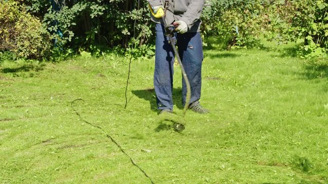 Faceless man in summer sandals mowing lawn with brush cutter. Leg, feet of male yardman in waterproof outdoor slippers who holds lawnmower. Gardener working on grassplot, backyard with grass trimmer