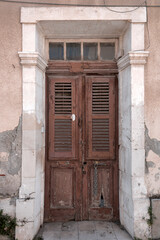 Old obsolete brown wooden front door with shutters in stone doorway