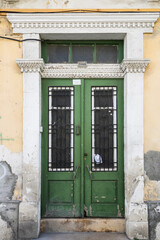 Green obsolete front door with glass panels and metal grates in old stucco wall
