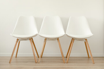 Three free white chairs against a white wall in an office or room, free space.