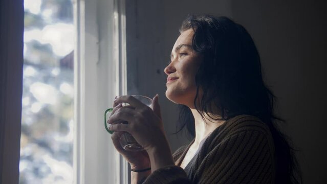 Woman drinking tea and looking out of window and smiling 