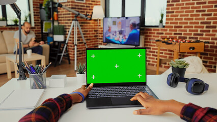 Young adult working on laptop with isolated green screen on display, showing chroma key background...