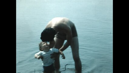 Testing the water 1951 - A toddler is reluctant to enter the water at Wilmette Beach, Illinois on Lake Michigan as his father lowers him, in 1951. 