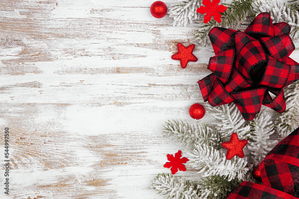 Poster christmas side border of red ornaments, snowy branches and red and black check plaid bow and ribbon.