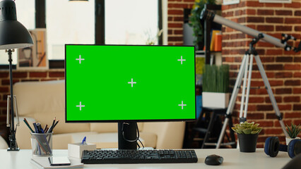 Fototapeta premium Empty desk with computer and greenscreen on monitor, showing chroma key display and isolated mockup template. Desktop pc screen with blank copy space background in living room.