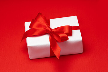Close up shot of gift box wrapped in white paper and decorated with ribbon bow isolated over bright colored red paper background