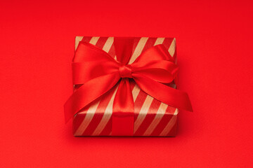 Close up shot of gift box wrapped in striped craft paper and decorated with satin ribbon bow, isolated on red background