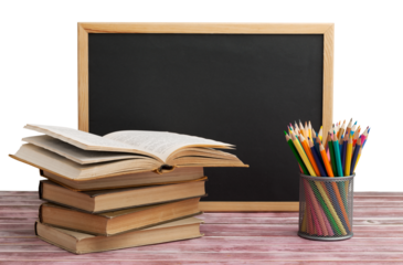 Stack of books with chalk blackboard and colored pencils on the wooden table.