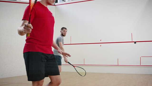 Young men play squash moving actively against front wall
