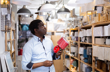 Portrait of interested focused african american man choosing light fixture for home interior design in furnishings store