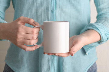 Female hand holding white mug with blank copy space for your advertising text message or promotional content. Girl in blue shirt holding white porcelain coffee mug mock up