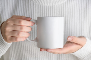 Female hand holding white mug mockup with blank copy space for your advertising text message or promotional content. Girl in blue shirt holding white porcelain coffee mug mock up