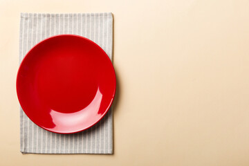 Top view on colored background empty round red plate on tablecloth for food. Empty dish on napkin with space for your design