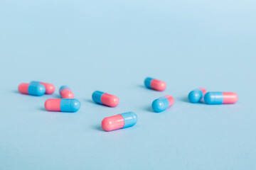 Obraz na płótnie Canvas Heap of pink and blue pills on colored background. Tablets scattered on a table. Pile of red soft gelatin capsule. Vitamins and dietary supplements concept