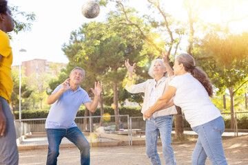 Social club of joyful older diverse people enjoying volleyball on the October sunny day outdoors
