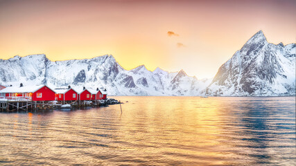 Traditional Norwegian red wooden houses (rorbuer) on the shore of  Reinefjorden near Hamnoy village at sunset.