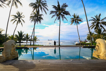 Stunning natural scenery, coconut trees on the beach with a blue swimming pool in the foreground and a bali beach background