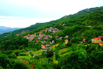 Vibrant landscape in Castel Trosino with numerous buildings perched on the rough hills of greenery with meadows and trees lying on them, some distant mountains in the background and a cloudy sky
