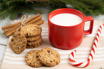 milk in a red mug and cookies on the table with Christmas tree branches, treats for Santa Claus, Christmas traditions, caramel cane