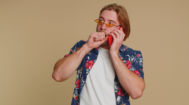 Tired Sleepy Freelancer Tourist Man Talking On Mobile Phone With Friend, Making Online Conversation. Disinterested Young Guy Boy Having Annoyed Boring Talk On Smartphone Isolated On Beige Background