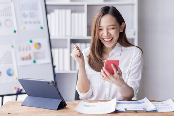 Happy Asian woman holding a smartphone and winning the prize, asian female happy excited in workplace office