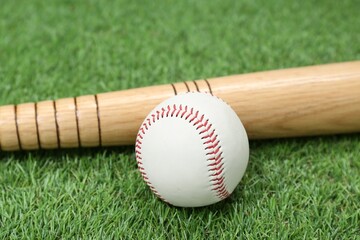 Obraz na płótnie Canvas Wooden baseball bat and ball on green grass, closeup. Sports equipment