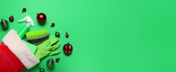 Santa hat with cleaning supplies and decor on green background with space for text. Christmas...
