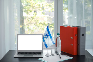 Modern laptop, flag of Israel, folders and bottle with water on table