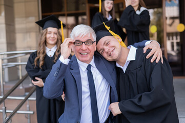 Father and son embrace at graduation. Parent congratulates university graduate.