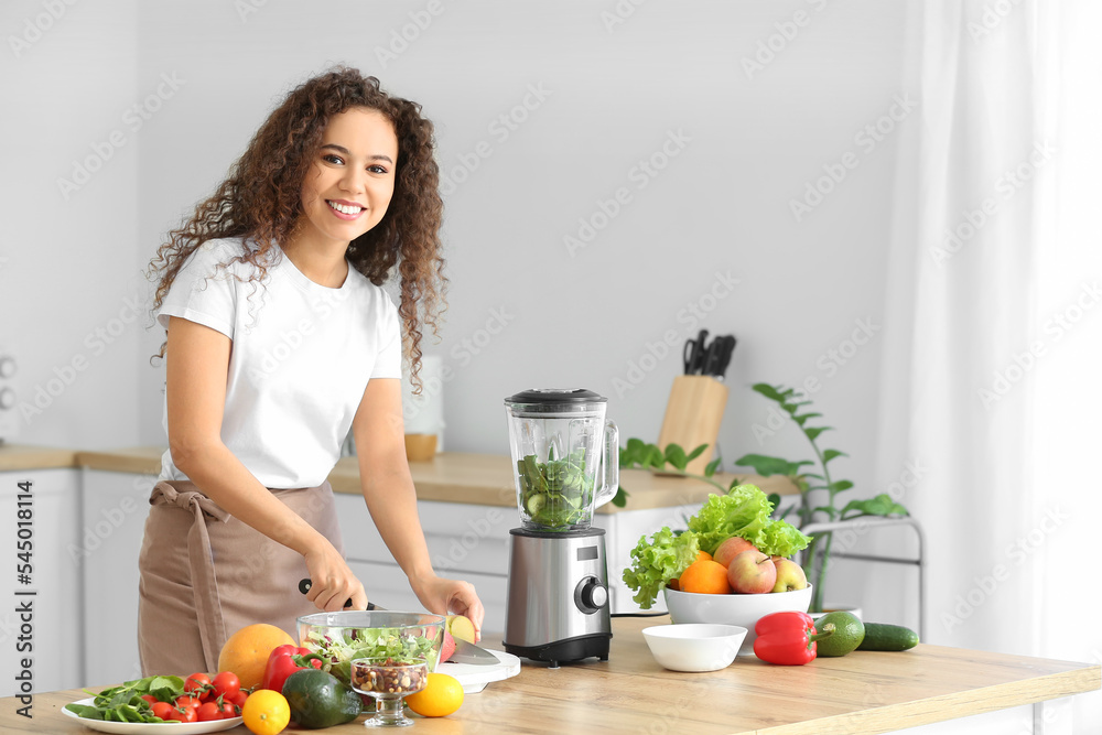 Wall mural Young African-American woman cutting products for smoothie in kitchen