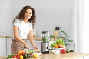 Young African-American woman cutting products for smoothie in kitchen