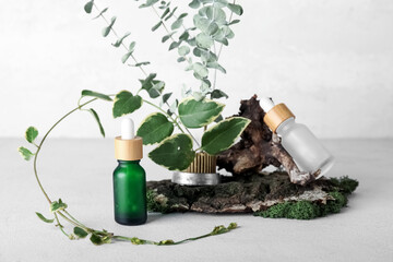 Cosmetic dropper bottles with ikebana, tree bark and green moss on light background