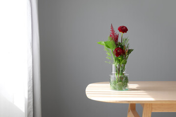Vase with beautiful ikebana on table near grey wall in room