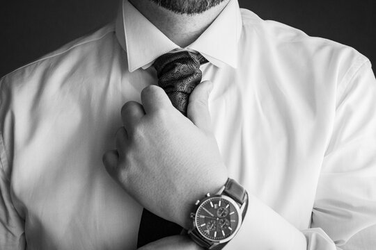 dettagli durante una cerimonia che ritrae lo sposo che si aggiusta la cravatta e mostra il dettaglio del collo , orologio da polso del suo matrimonio  in bianco e nero