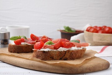 Tasty bruschettas with prosciutto, tomatoes and cheese on white wooden table