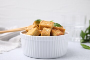Bowl with delicious fried tofu, basil and sesame seeds on white table