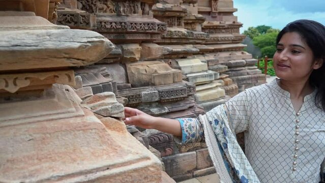 Beautiful Indian Woman Walking And Admiring Carved Stones Outside Temple Of Khajuraho In Madhya Pradesh, India. medium shot