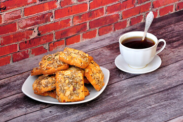 A plate with a bunch of fresh shortbread cookies with peanuts and cumin on a wooden table, next to a cup of hot black tea.