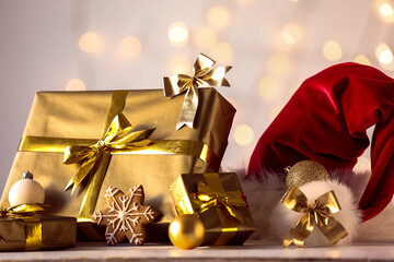 Beautiful Christmas gifts, decorations and Santa hat on table against blurred lights, closeup