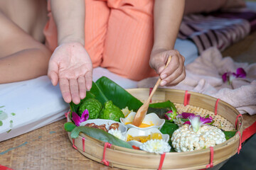 An elderly Asian woman receives a pain-relieving massage by a herbal therapist in a traditional Thai position.